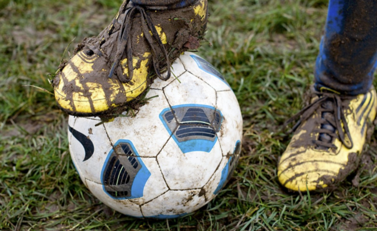 Close up of a muddy football shoe standing on muddy football on a muddy field.