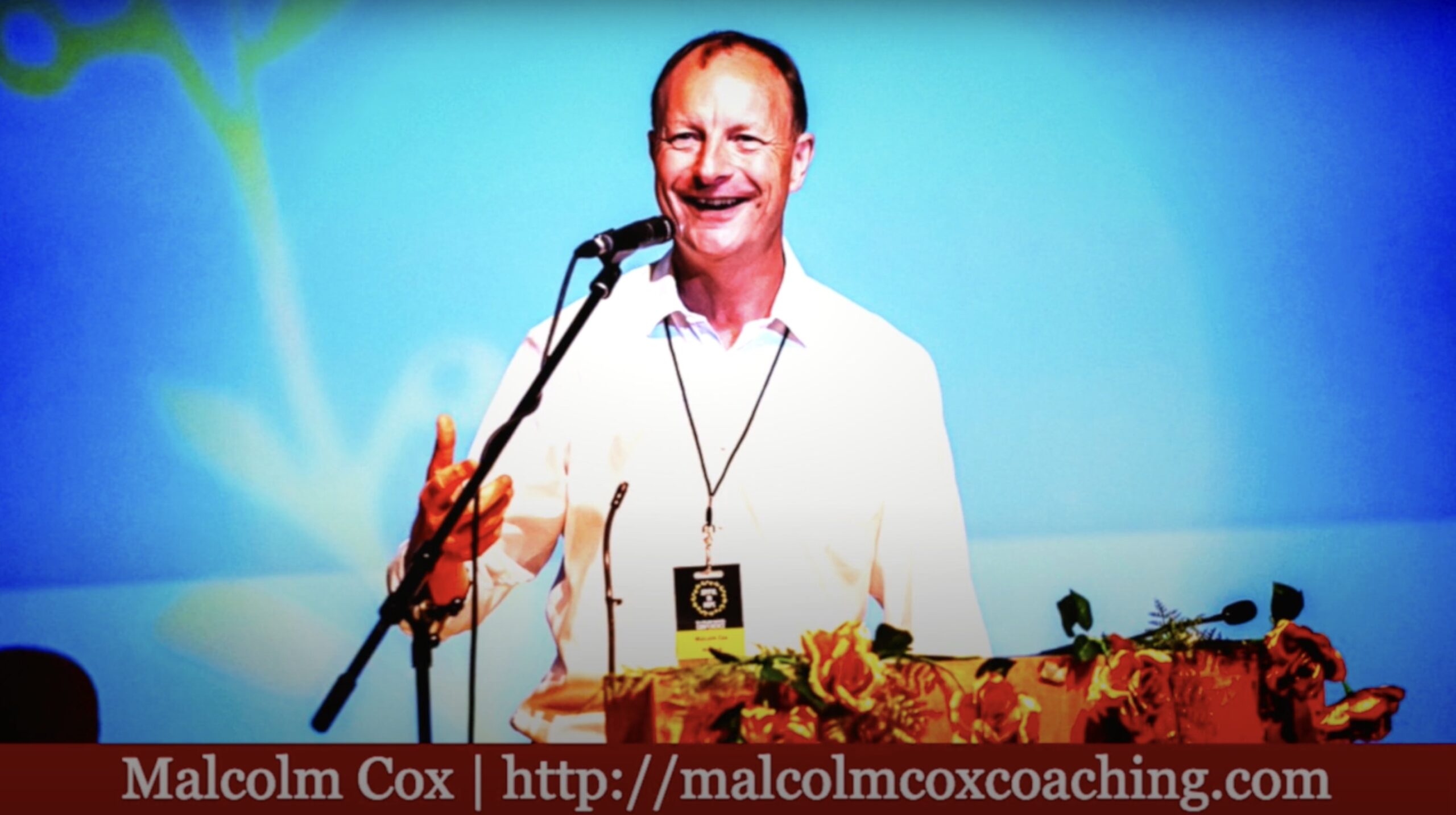 Malcolm Cox standing at a podium giving a talk.